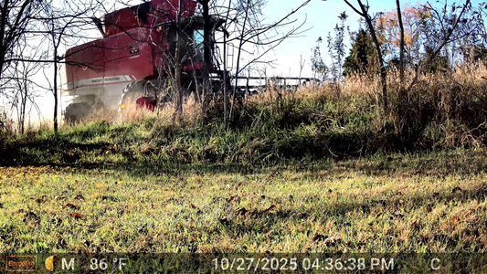 Red combine harvester captured by a long-range wireless trail camera, monitoring farm equipment movement across a large property